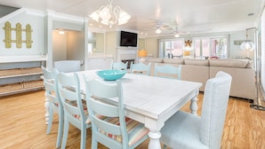A spacious living room with a white dining table, light blue chairs, and a beige sofa.