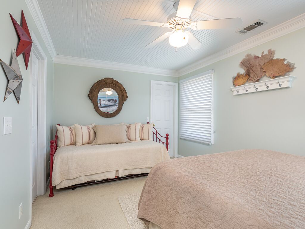A bedroom with two beds, a ceiling fan, a mirror, and a wall-mounted shelf with decorative items.