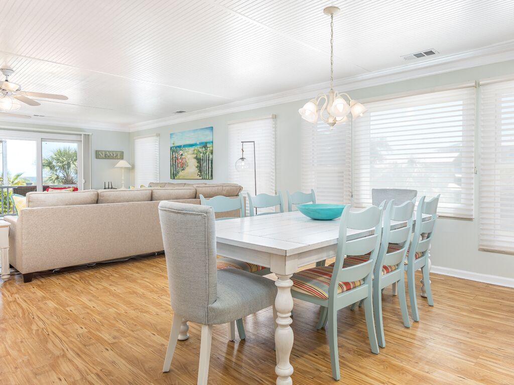 A spacious living room with a large sofa, a dining table with chairs, and a ceiling fan.