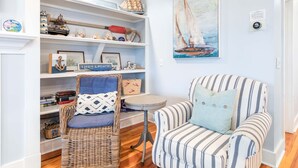 Une pièce chaleureuse avec un fauteuil à rayures, une chaise en osier et des étagères décorées sur le thème de la marine.