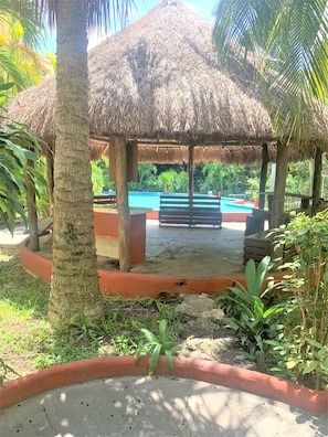 A thatched-roof gazebo with a pool and benches in a tropical setting. - Villa Aida (CANCUN)