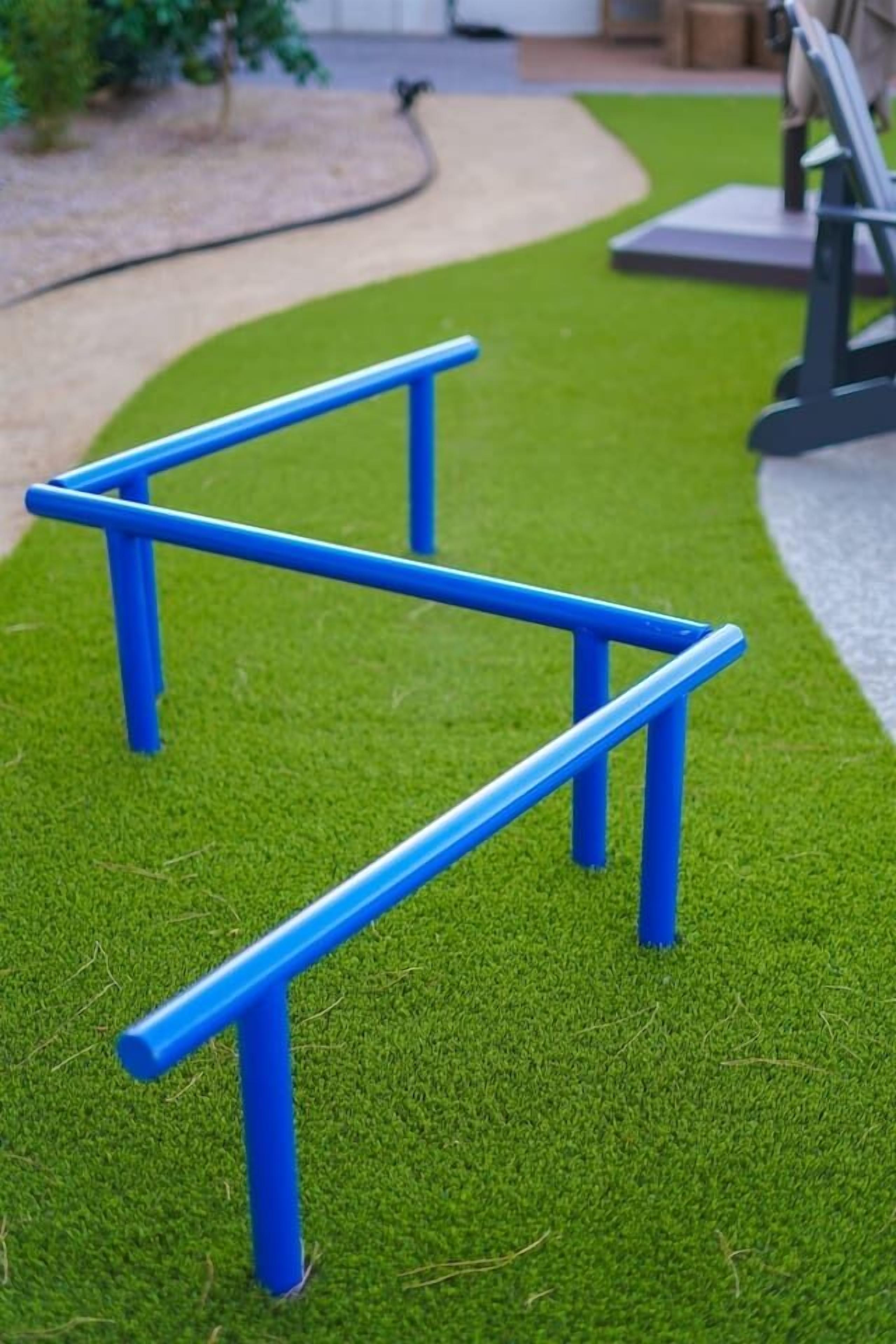 Estrutura metálica azul sobre grama sintética, provavelmente equipamento de exercícios para uso externo.