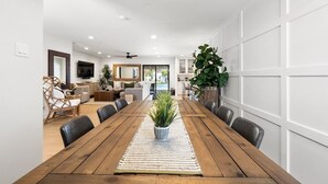 A spacious dining area with a wooden table, surrounded by chairs, and a large potted plant in the center. - Upscale Oasis | Pool, Putting Green, Volley Court & Open Yard (Scottsdale)
