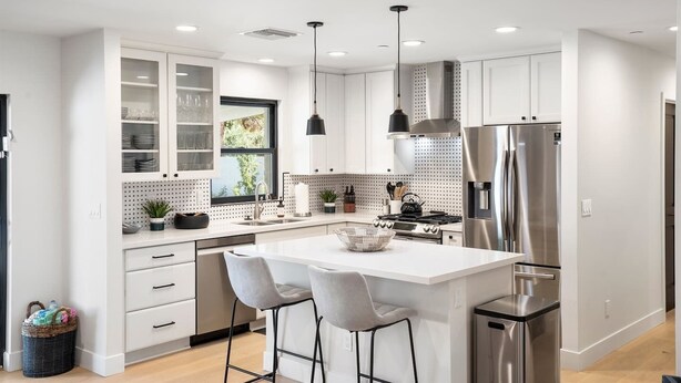 A modern kitchen with white cabinets, stainless steel appliances, and a central island with bar stools. - Upscale Oasis | Pool, Putting Green, Volley Court & Open Yard (Scottsdale)