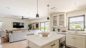 A modern kitchen with white cabinetry, a large island, and a dining area with a sofa. - Upscale Oasis | Pool, Putting Green, Volley Court & Open Yard (Scottsdale)