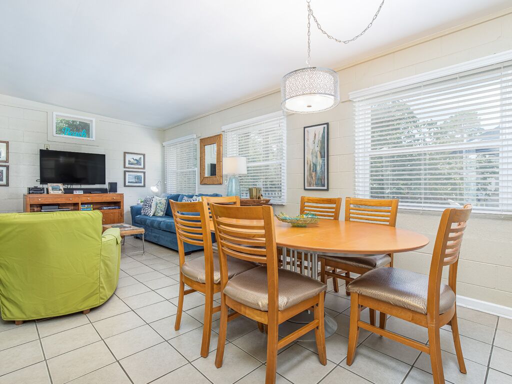 A dining area with a round table and six chairs, a green sofa, a television, and framed pictures on the walls.