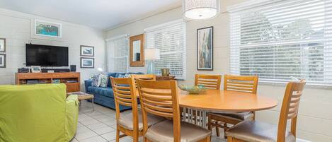 A dining area with a round table and six chairs, a green sofa, a television, and framed pictures on the walls.