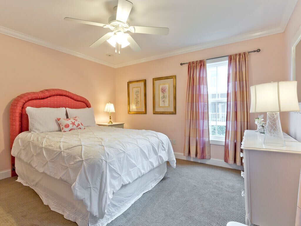 A bedroom with a bed, a ceiling fan, a nightstand, a lamp, and a window with curtains.