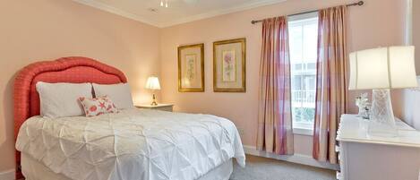 A bedroom with a bed, a ceiling fan, a nightstand, a lamp, and a window with curtains.