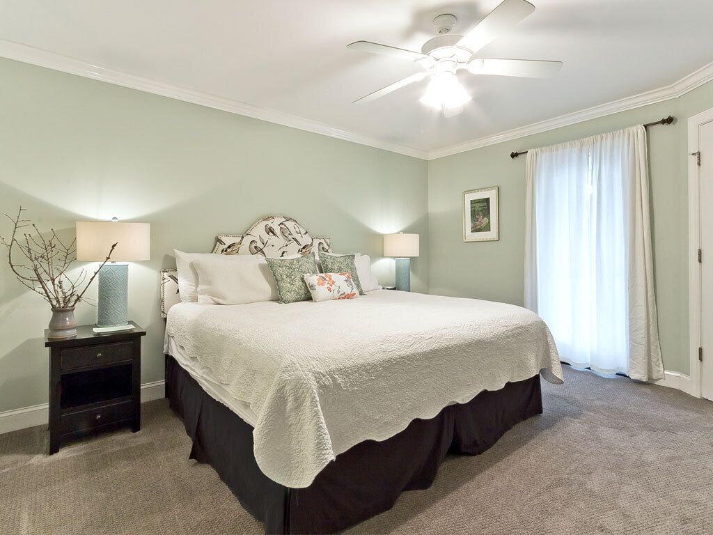 A bedroom with a bed, nightstands, a ceiling fan, and a window with curtains.