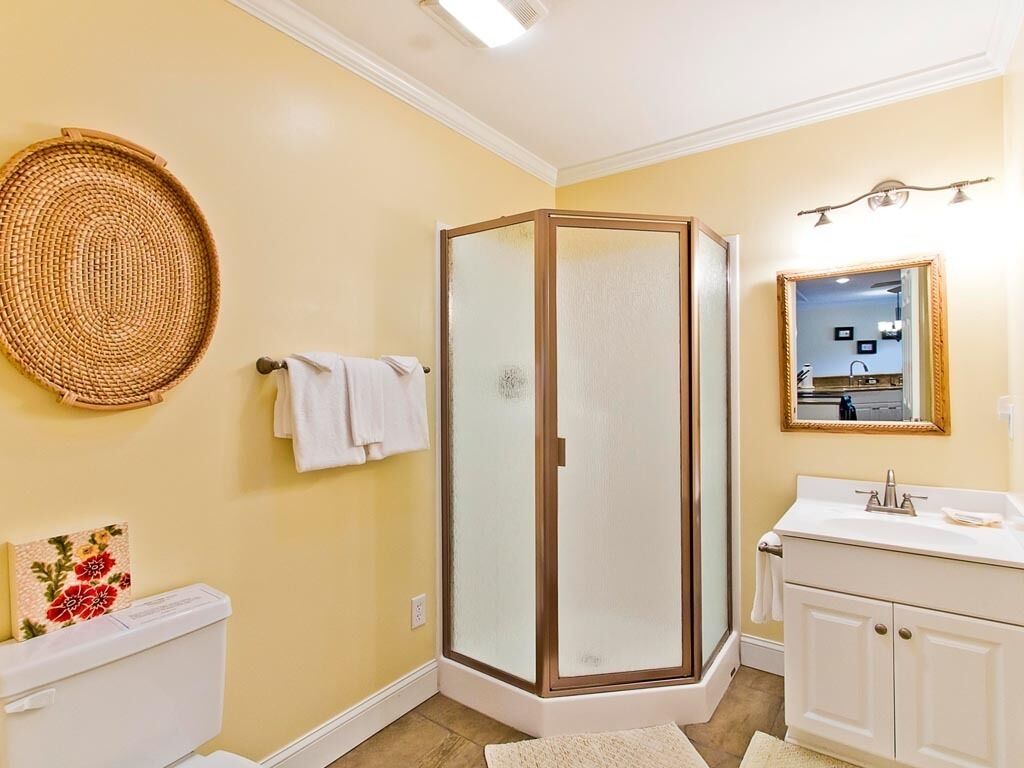 A bathroom with a glass-enclosed shower, a toilet, a sink with a mirror, and a decorative woven basket on the wall.