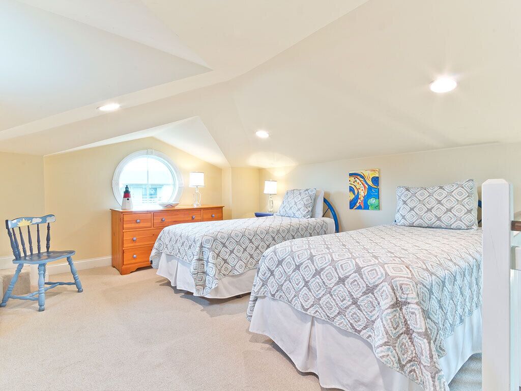 A bedroom with two beds, a dresser, a chair, and a window.