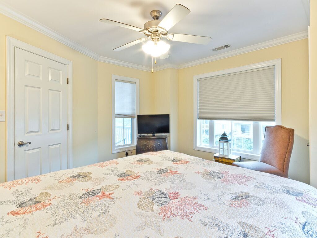 A bedroom with a bed, a ceiling fan, a television, and a window with blinds.