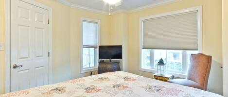 A bedroom with a bed, a ceiling fan, a television, and a window with blinds.