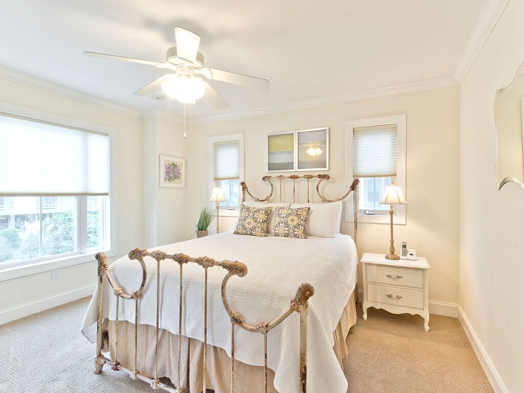 A bedroom with a bed, a nightstand, a ceiling fan, and a window with blinds.