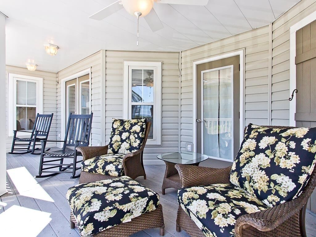 A covered porch with wicker furniture and a glass table.