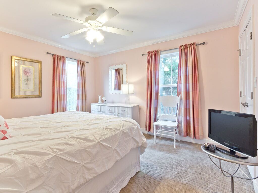 Une chambre à coucher avec un lit, une télévision, un ventilateur de plafond et une fenêtre avec des rideaux.