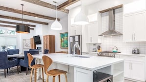A modern kitchen with white cabinetry, a central island with stools, a built-in oven, and pendant lighting. - Savannah Jetsetter by Tybee Vacation Rentals (Savannah)