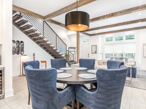 A dining area with a round table and six chairs, a staircase, and a modern pendant light.