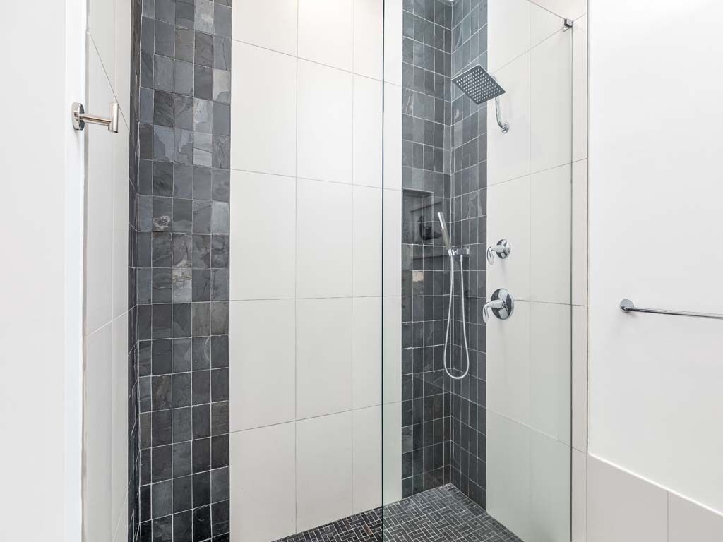 A modern shower with a glass door, a showerhead, and a handheld shower attachment.