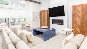 A modern living room with a sectional sofa, a coffee table, a flat-screen TV, and a fireplace. - Savannah Jetsetter by Tybee Vacation Rentals (Savannah)