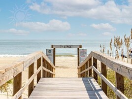 A wooden boardwalk leading to a beach with a sign reading "7th Street" and beach rules posted.