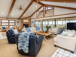 A spacious living room with a high ceiling, large windows, and a fireplace.