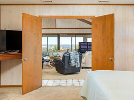 A bedroom with a large bed, a desk with a TV, and a view of the outdoors.