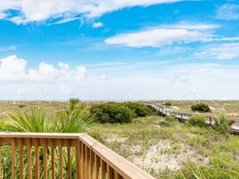 A wooden deck overlooking a coastal landscape with a wooden walkway and sparse vegetation.