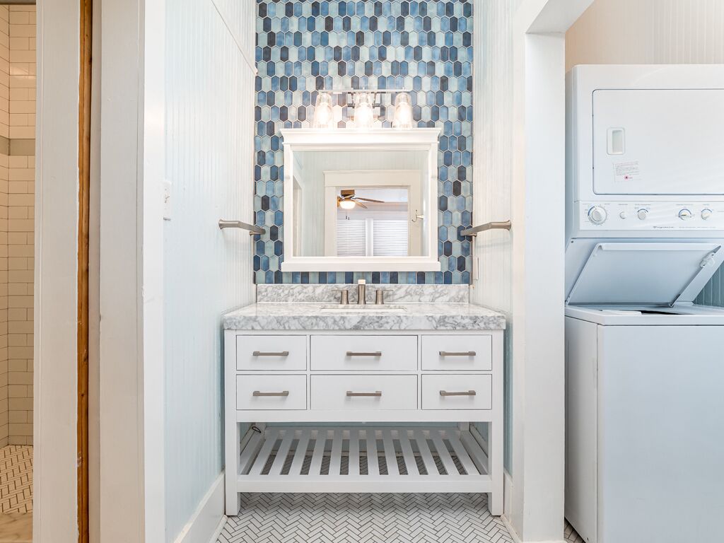 A bathroom with a white vanity, a tiled backsplash, and a washing machine.