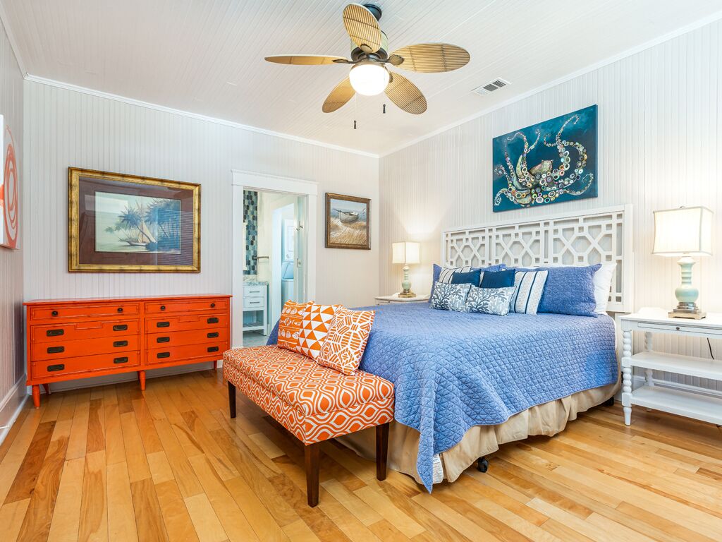 Ein Schlafzimmer mit Bett, Deckenventilator, Kommode und Bildern an den Wänden.