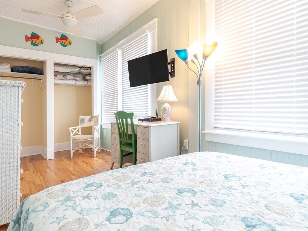 A bedroom with a bed, a desk, a chair, a television, and a window with blinds.