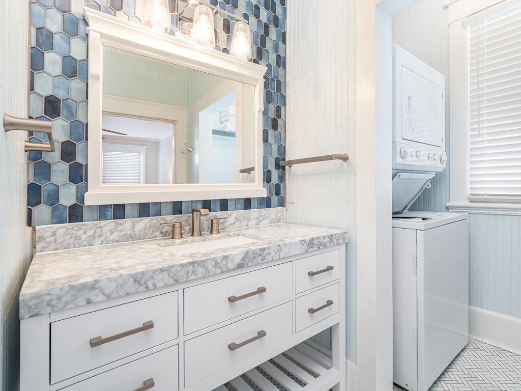 A bathroom with a marble sink, a mirror, and a tiled backsplash.