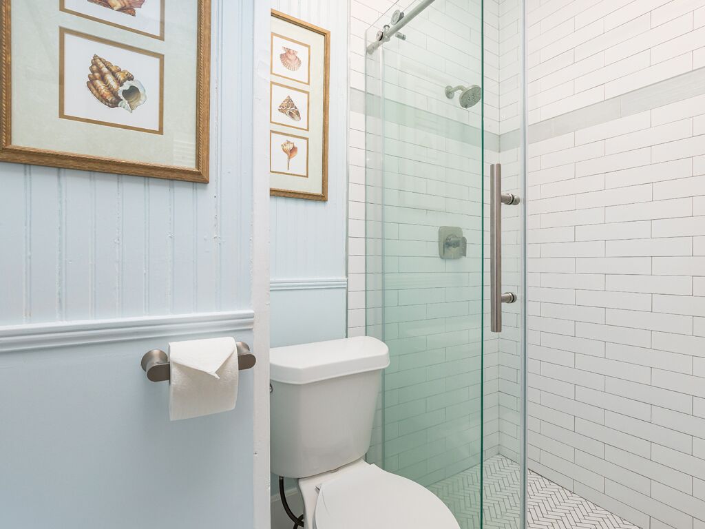A bathroom with a toilet, a glass shower enclosure, and framed pictures on the wall.