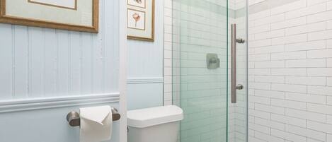 A bathroom with a toilet, a glass shower enclosure, and framed pictures on the wall.