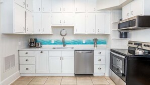 A modern kitchen with white cabinets, a stainless steel dishwasher, a black stove, and a microwave. - Sea View 2 by Tybee Vacation Rentals (Tybee Island)