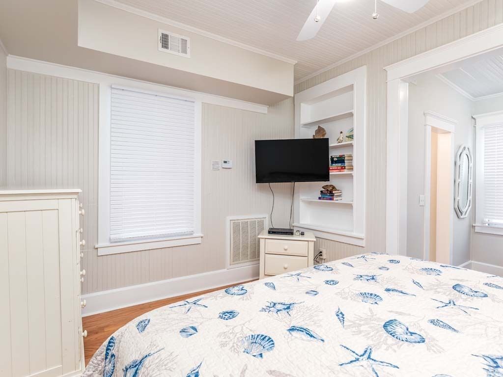 A bedroom with a bed, a television, a nightstand, and a shelf with books and decorative items.