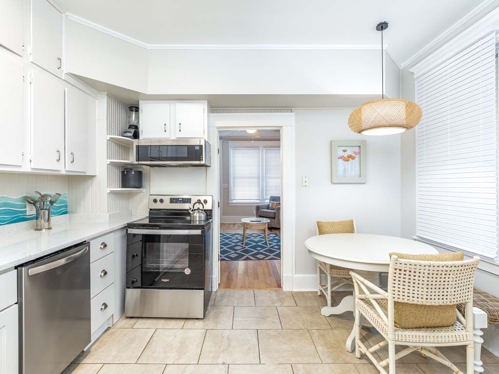 A modern kitchen with white cabinetry, a built-in oven, and a dining area with wicker chairs.
