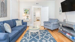 A living room with a blue sofa, a grey armchair, a coffee table, and a flat-screen TV. - Sea View 2 by Tybee Vacation Rentals (Tybee Island)