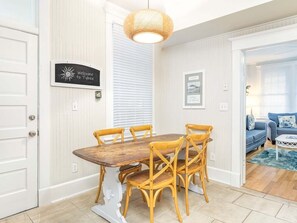 Uma área de refeições com mesa de madeira e quatro cadeiras, luminária pendente e um letreiro na parede.