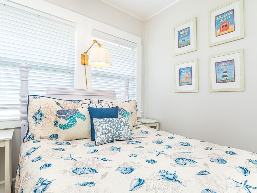 Un dormitorio con una cama que incluye una colcha con motivos náuticos, una lámpara de noche y carteles enmarcados con temática marina en la pared.