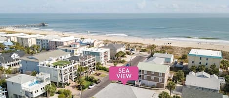 An aerial view of a coastal residential area with buildings, a beach, and a pier.