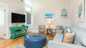Un salon comprenant un téléviseur, un meuble de rangement turquoise, un pouf bleu et un canapé bleu clair.