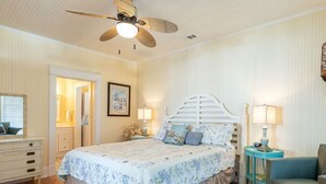 A bedroom with a bed, a ceiling fan, a nightstand, a chair, and a dresser. - Sea View Cottage by Tybee Vacation Rentals (Tybee Island)