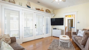 A spacious living room with a ceiling fan, a flat-screen TV, a white coffee table, and a brown sofa. - Sea View Cottage by Tybee Vacation Rentals (Tybee Island)