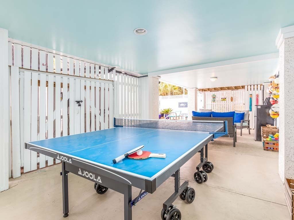 A ping pong table with a table tennis paddle and ball, a blue sofa, and a white fence in the background.