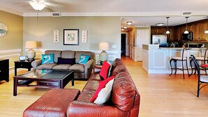 A spacious living room with a leather sofa, a coffee table, and a dining area with wooden cabinets and a kitchen island. - Silver Seas 203 by Tybee Vacation Rentals (Tybee Island)