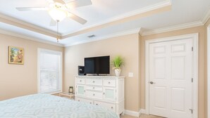 A bedroom with a bed, a ceiling fan, a TV on a dresser, a door, and a window with blinds. - Silver Seas 203 by Tybee Vacation Rentals (Tybee Island)