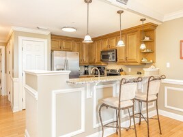 Una cocina con armarios de madera, un refrigerador de acero inoxidable, un microondas y una barra con dos taburetes.