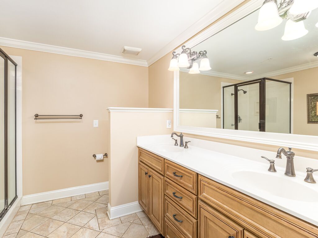 A bathroom with beige walls, a white vanity with a large mirror, and a shower area.